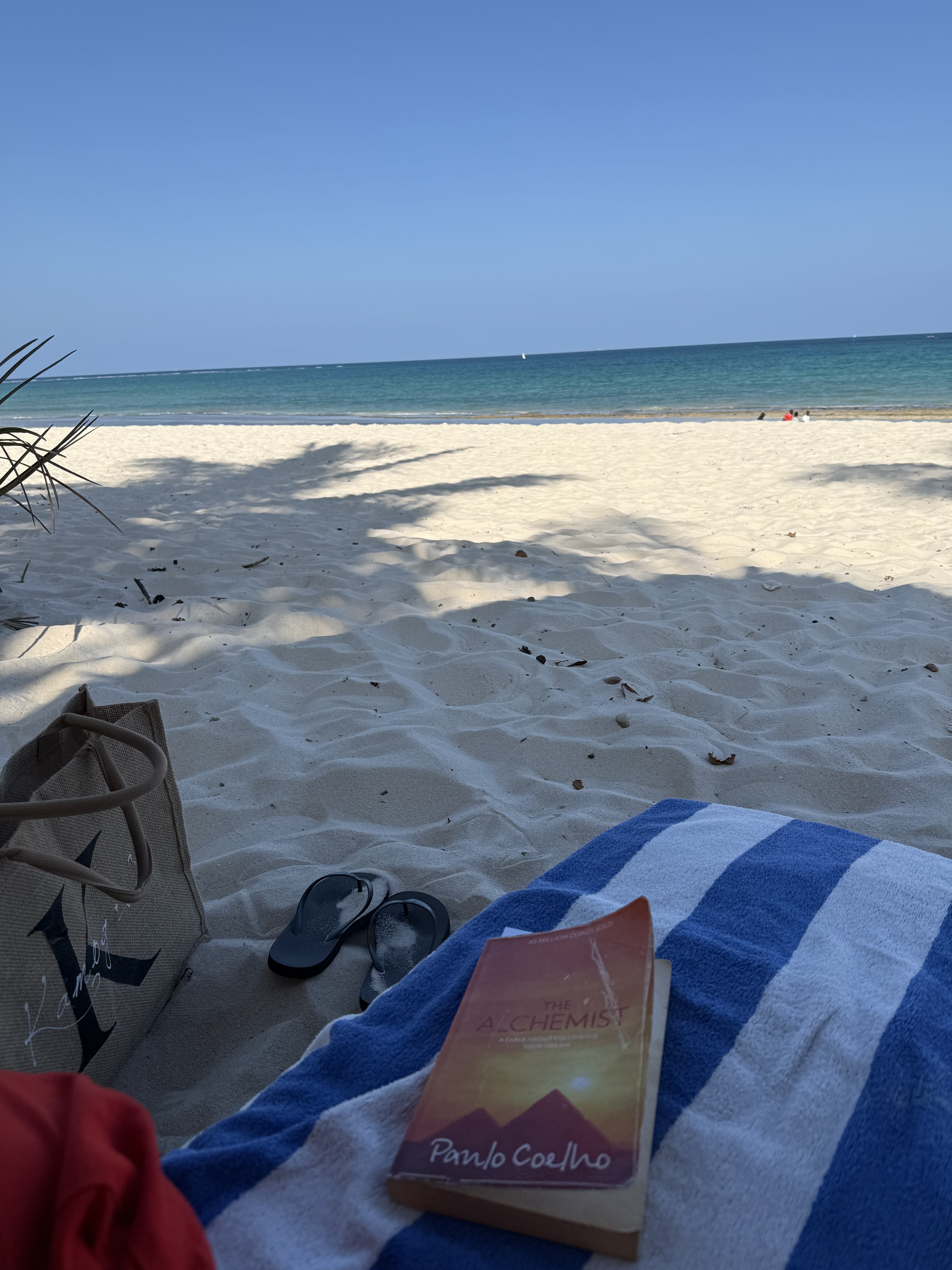 Beach day with a book and sandals on the white sand